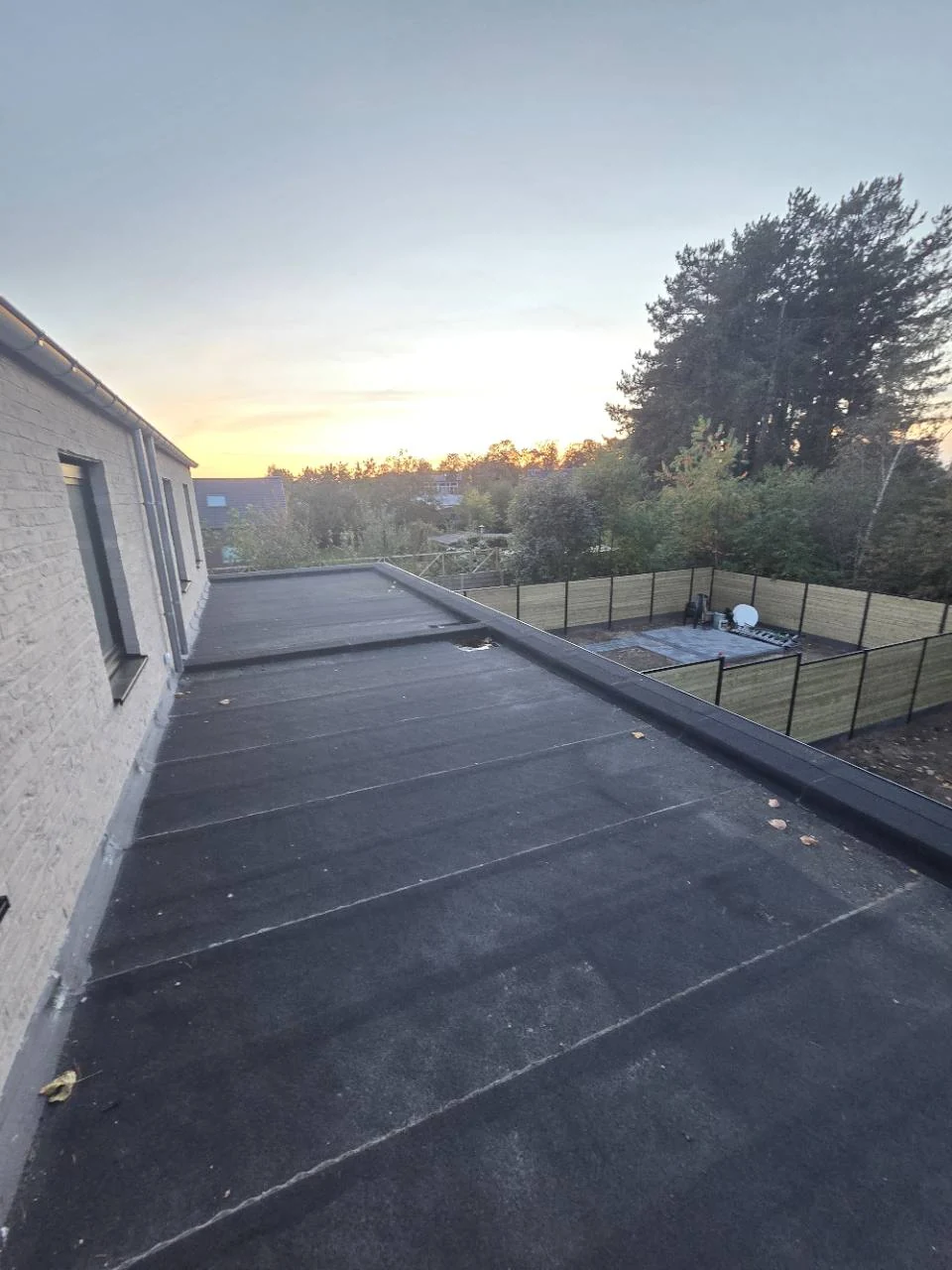 Aangeleverde werffoto met een plat bitumendak langs de gevel en afgewerkte dakrand.